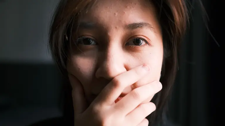A thoughtful close-up portrait of a person covering their mouth with a hand, expressing emotion.