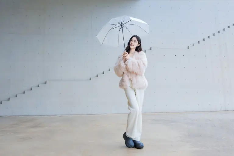 Stylish woman in faux fur coat with umbrella in modern minimalist indoor setting.