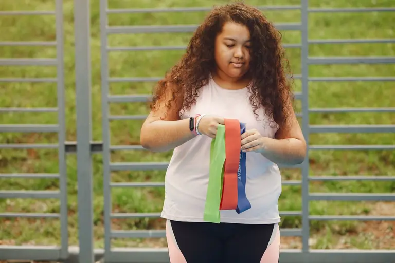 A young woman with curly hair holds resistance bands during an outdoor workout session.