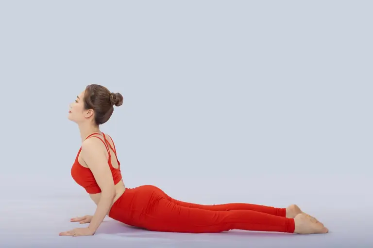 A woman in vibrant red sportswear performing the cobra yoga pose in a studio setting.