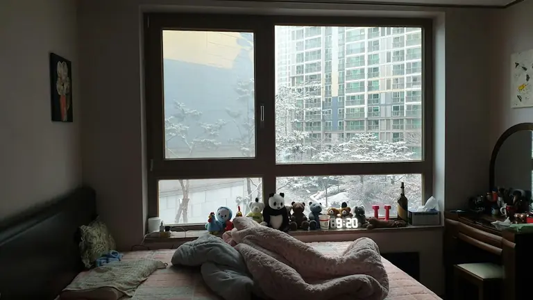 A bedroom with a bed, desk and a large window