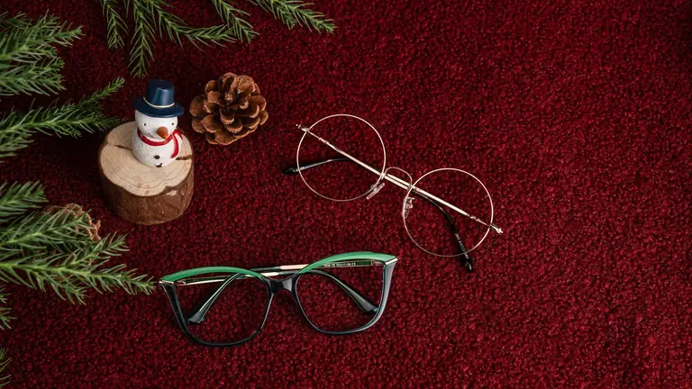 Two pairs of stylish glasses with holiday decor including a snowman and pinecones on red background.