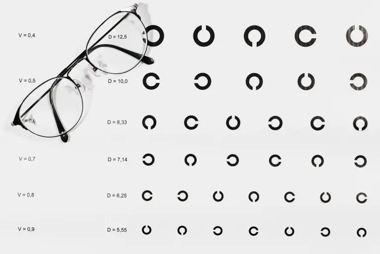 Close-up of eyeglasses placed on visual acuity test chart, symbolizing vision testing.