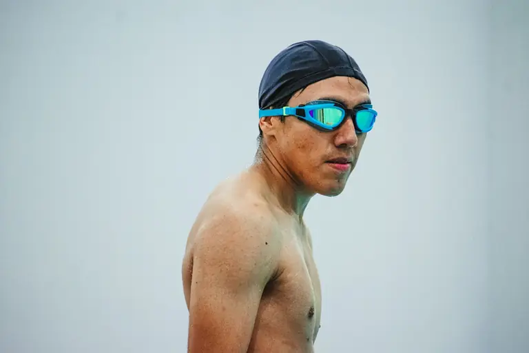 Focused male swimmer with swim cap and goggles ready for competition.