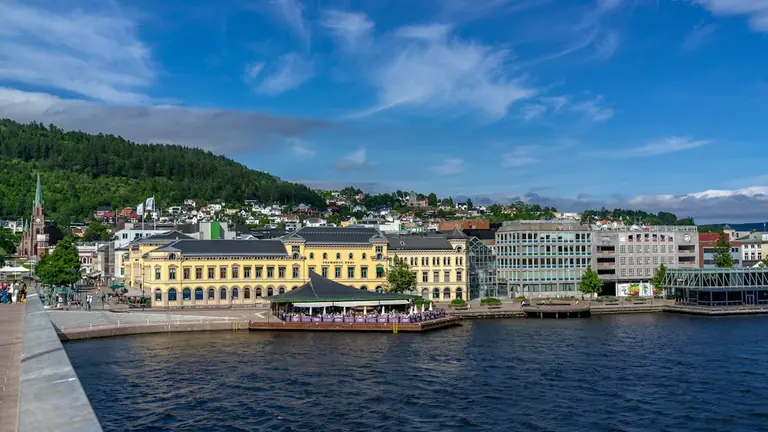 Scenic waterfront city with yellow buildings and lush green mountains.