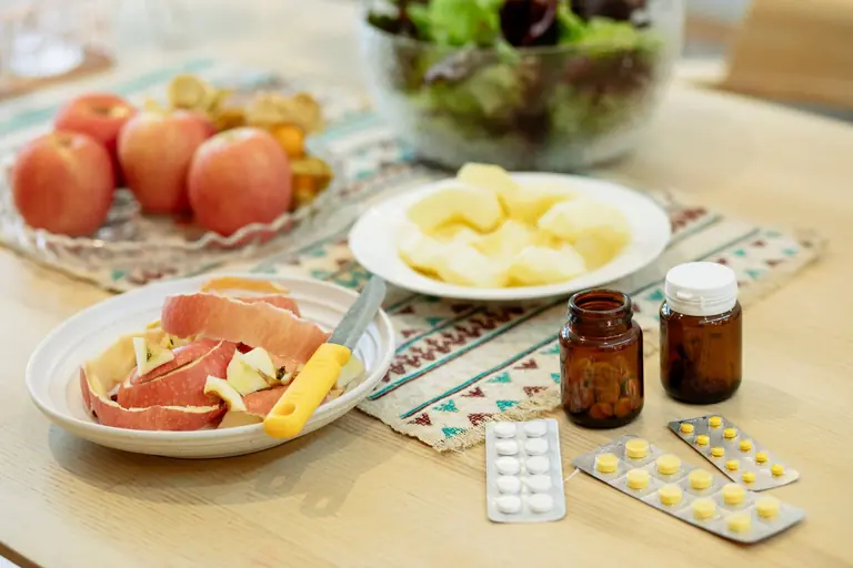 From above of various medicines placed on table near plates with fresh peeled apples and bowl of salad in kitchen