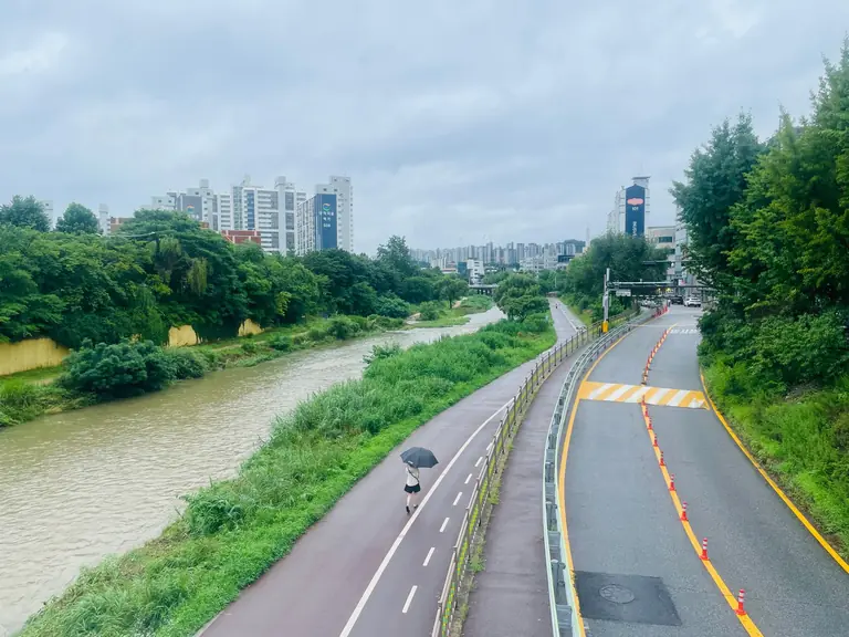 A person walks with an umbrella on a riverside path in Seoul, South Korea.