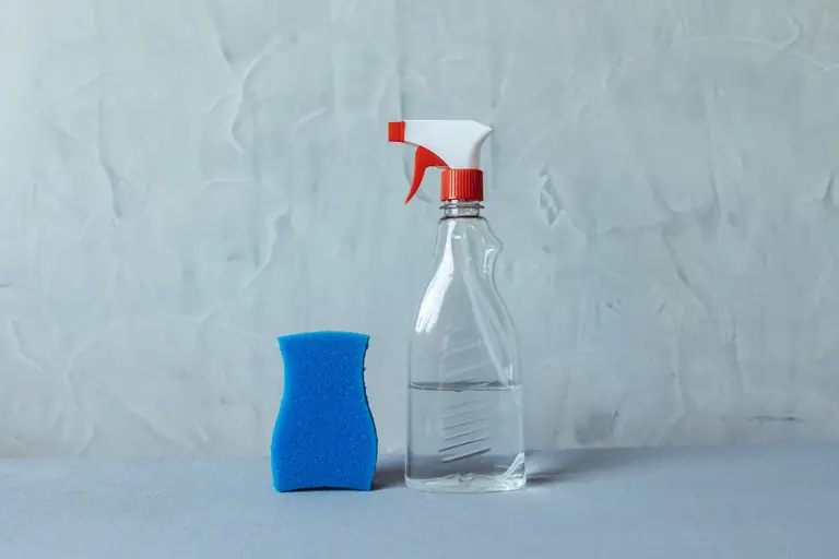 A spray bottle and blue sponge on a textured grey surface. Perfect for cleaning themes.