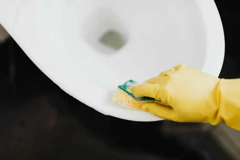 From above of crop unrecognizable person wearing yellow rubber gloves disinfecting and cleaning toilet bowl with sponge in bathroom