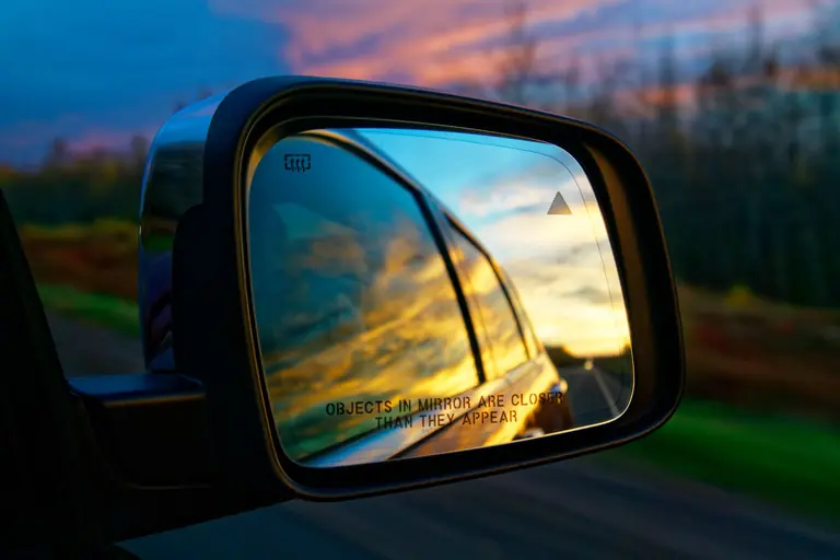 A car side mirror reflecting a vibrant sunset sky on a highway, creating a colorful and dynamic travel scene.