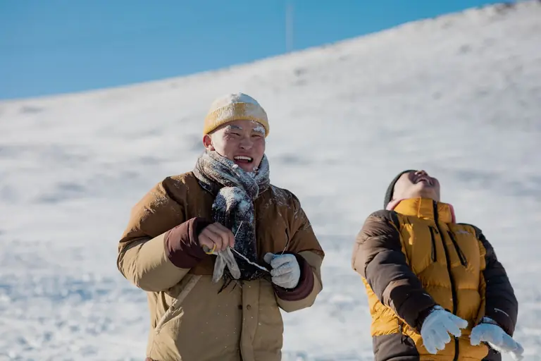 Two adults enjoy a fun-filled winter day on a snowy mountainside, laughing and bundled up.