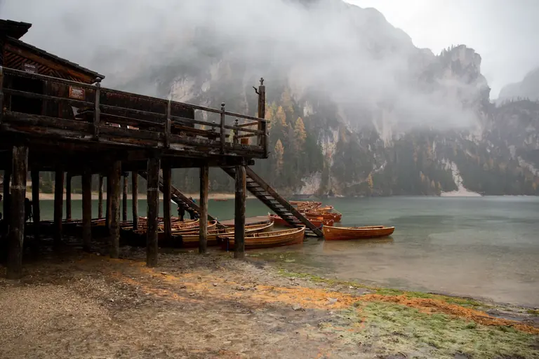 Serene and misty lakeside view with wooden boats and dock amidst mountains and fog.