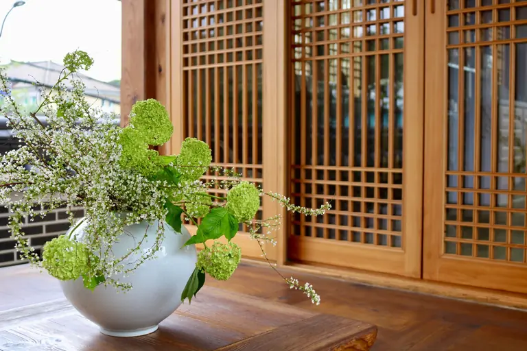 A stunning vase with green and white flowers on a wooden table in a traditional Korean setting.