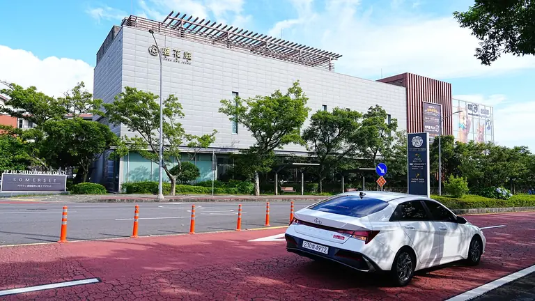 White sedan car parked near modern building with trees and clear sky in Jeju, South Korea.