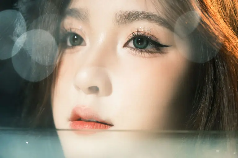 Artistic close-up of a woman's face with light bokeh and serene expression, emphasizing elegance.