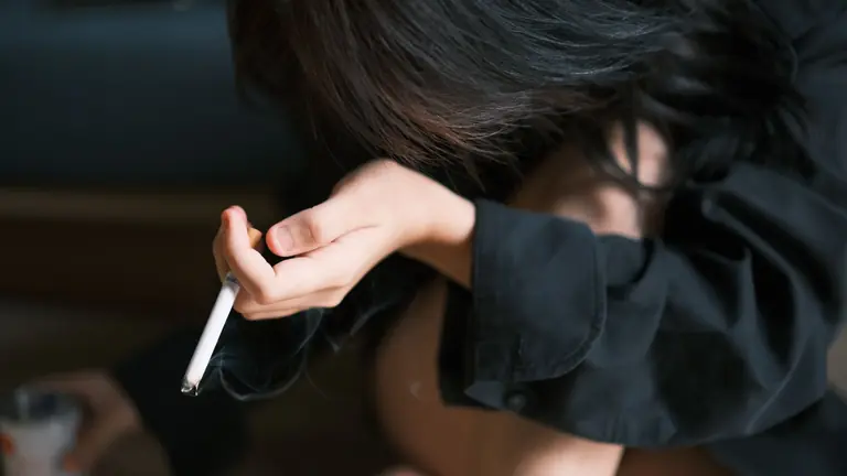 Close-up of a young woman holding a cigarette, indoors in a contemplative pose.