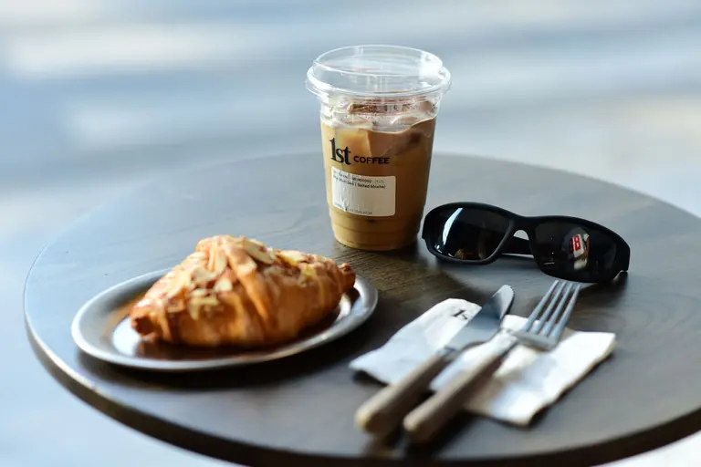 Cup of iced coffee and croissant on a table with sunglasses, offering a relaxed café vibe.