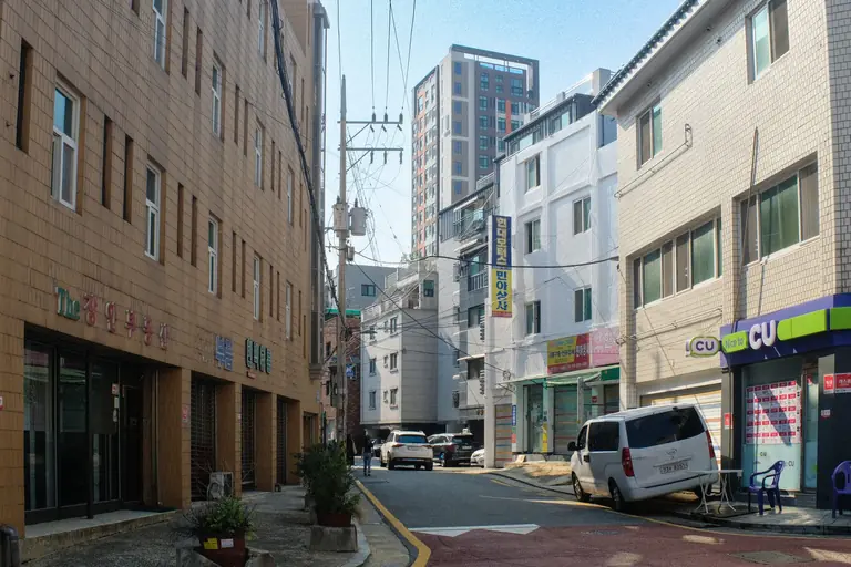 A city street in Seoul, South Korea featuring modern buildings and parked vehicles on a sunny day.