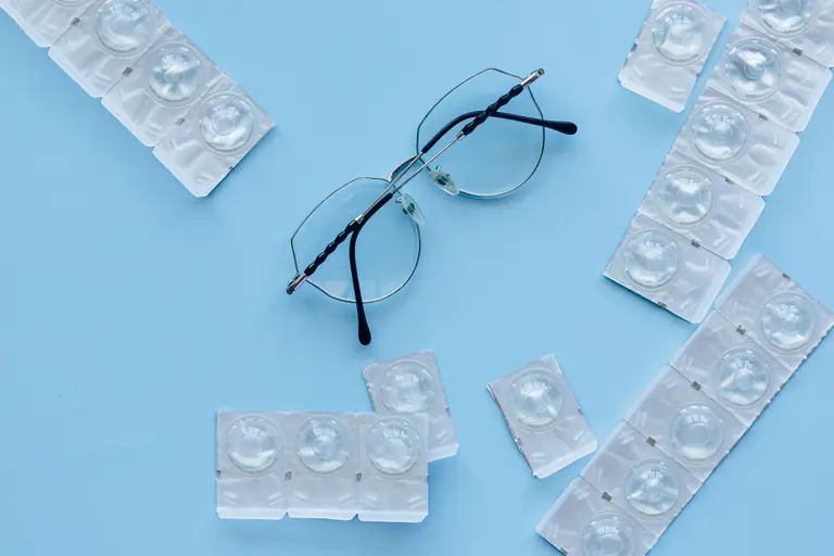 Eyeglasses and contact lenses on a blue background. Concept of eye care and vision correction.