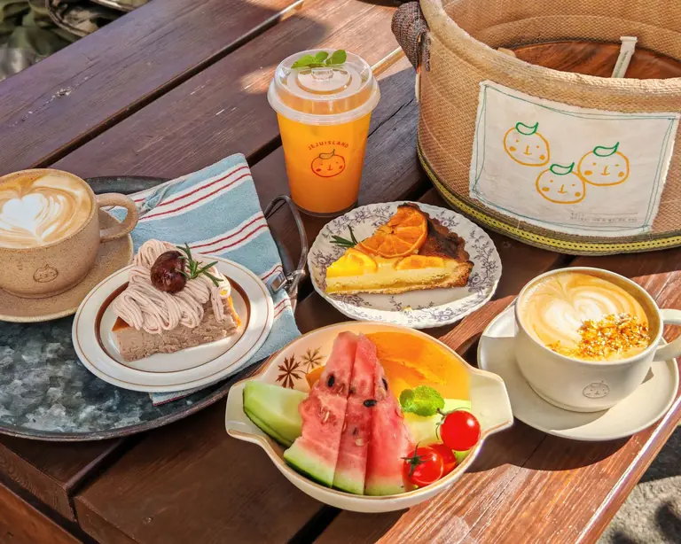 A delicious breakfast spread outdoors featuring coffee, juice, fruit, and cakes on a sunny day.