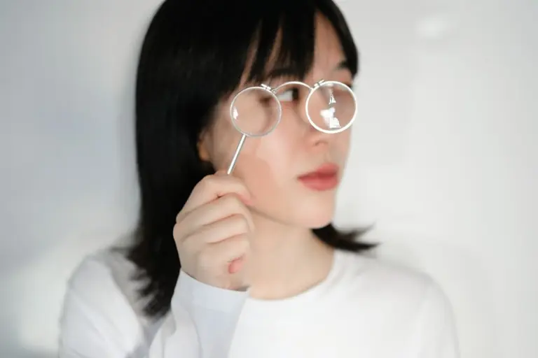 A person holding a pair of round silver spectacles in front of one eye
