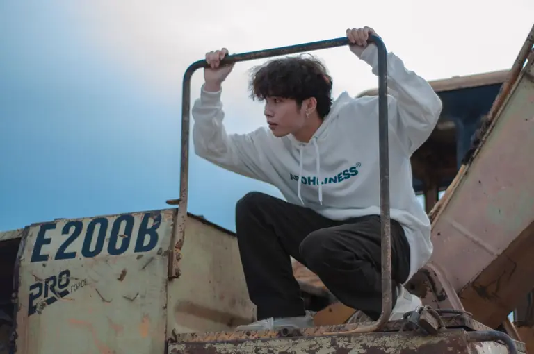 A young man poses on industrial machinery in an urban setting, exuding a modern and stylish vibe.
