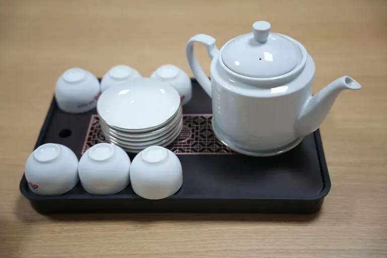 White ceramic teapot with matching cups and saucers on a tray. Perfect for afternoon tea settings.