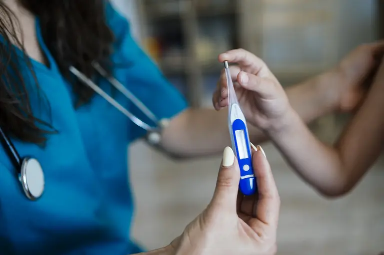 Nurse checks child's temperature with digital thermometer in a clinical setting