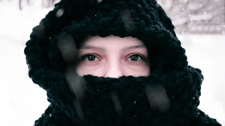 Close-up of a person bundled in winter clothing, highlighting expressive eyes.