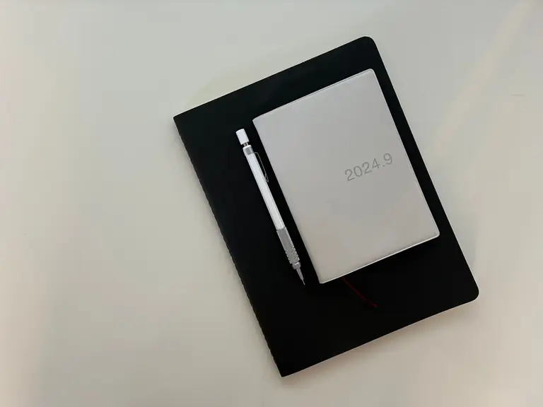 Flat lay of a notebook with a pen and planner on a white table.