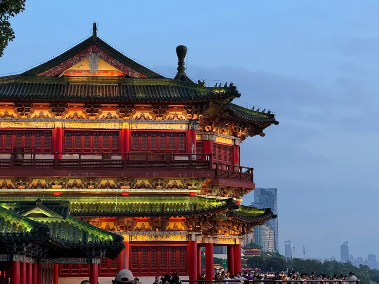 Stunning traditional Chinese pavilion illuminated at twilight with urban skyline backdrop.