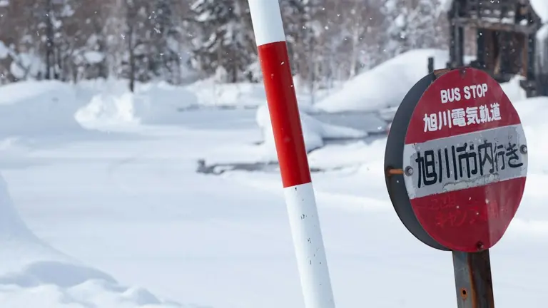 A red and white sign sitting on the side of a snow covered road