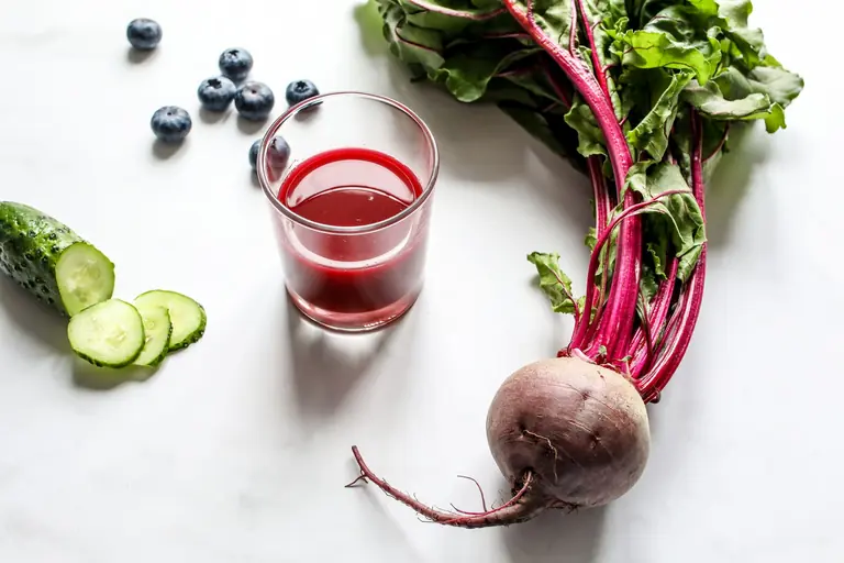Nutrient-rich beetroot, cucumber, and blueberry juice with fresh produce on white background.