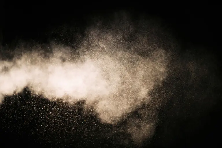 Dynamic view of dust particles in motion, illuminated against a black background, creating an ethereal effect.