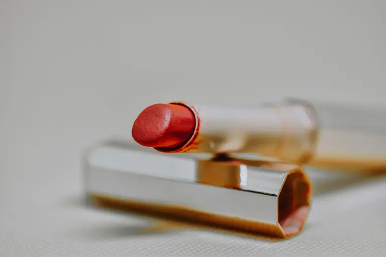 Sophisticated close-up shot of a red lipstick with reflective case on a neutral background, highlighting beauty and elegance.