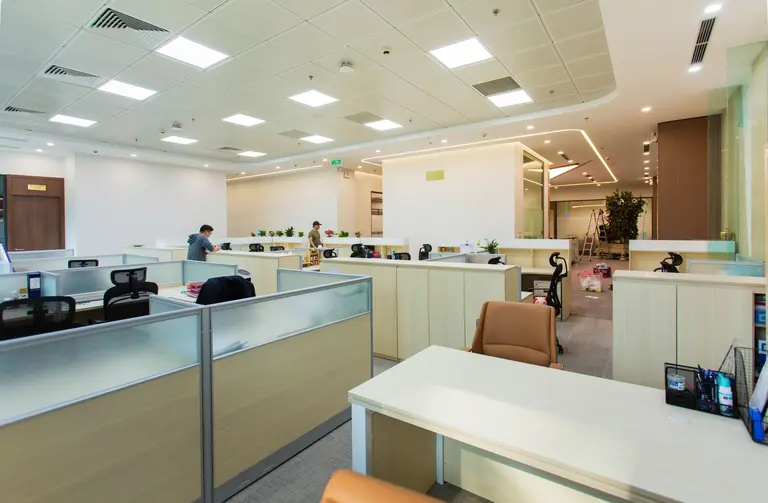 Bright and spacious office interior featuring open-plan cubicles, modern furniture, and ceiling lights.