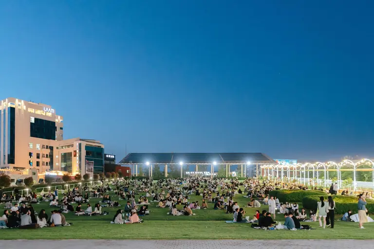 A vibrant evening event in an illuminated urban park in Gwangju, South Korea, with people enjoying leisure activities.