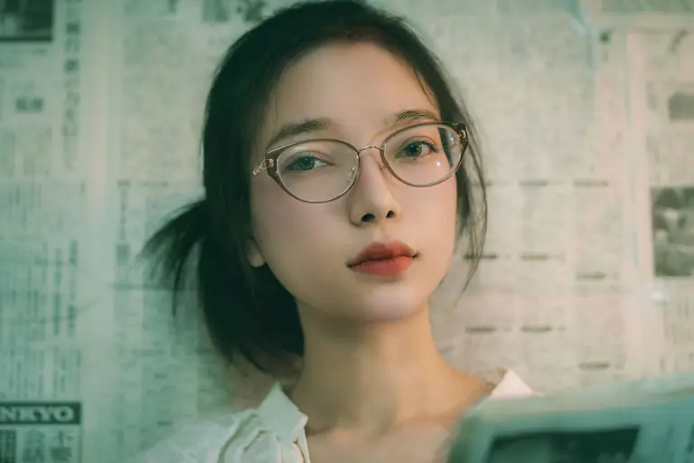 Close-up portrait of a young woman wearing glasses, gazing calmly at the camera.