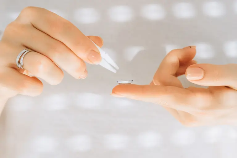 Close-up of female hands carefully handling a contact lens with a tweezer.