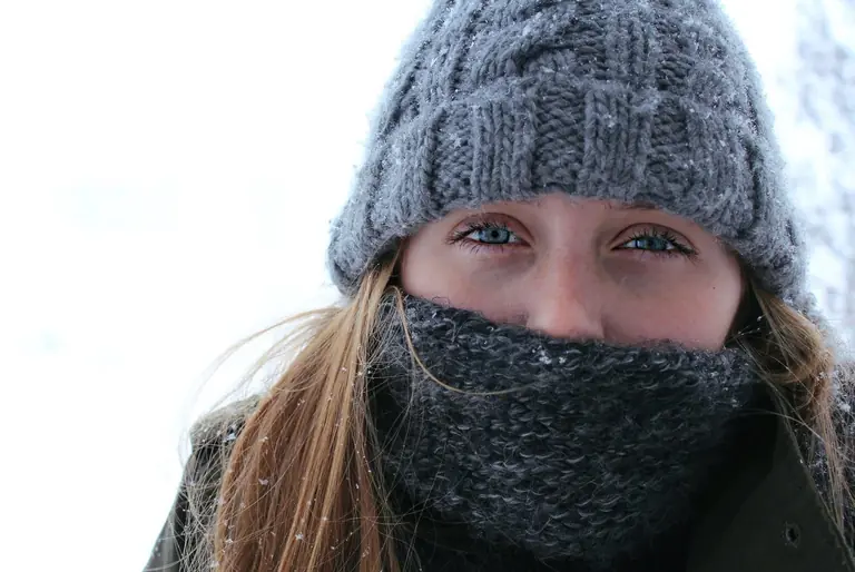A young woman in a warm knit hat and scarf during a snowy winter day.