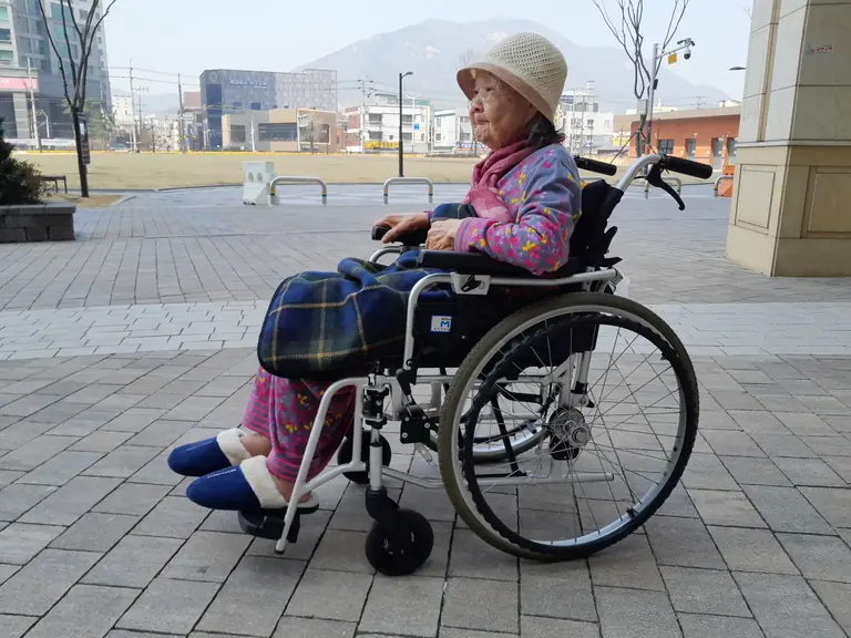 Elderly woman sitting in a wheelchair outdoors, showcasing independence and urban life.