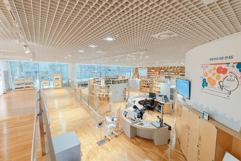 Open and airy modern library with bookshelves, desks, and a large screen in a well-lit space.