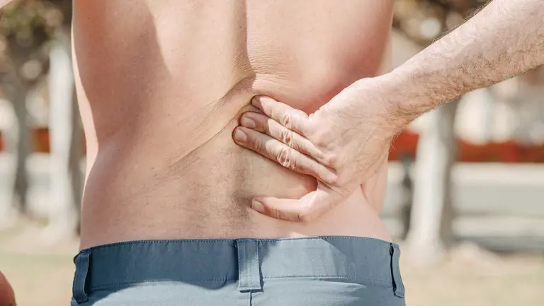 Close-up of a man holding his lower back in pain, possibly indicating discomfort or injury.